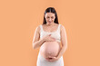 © New Africa - Pregnant woman touching her belly on orange background