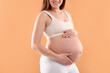 © New Africa - Pregnant woman touching her belly on orange background, closeup