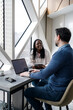 © Marko - Two people have a conversation at a desk near a window in a modern office setting
