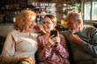 © Geber86 - Happy grandparents and teen girl using smartphone at home