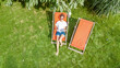 © Iuliia Sokolovska - Young girl relaxes and reading book in summer garden in sunbed deckchair on grass, relaxing outdoors in green park on weekend, aerial drone view from above