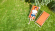 © Iuliia Sokolovska - Young girl relaxes and reading book in summer garden in sunbed deckchair on grass, relaxing outdoors in green park on weekend, aerial drone view from above