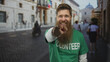 © Krakenimages.com - Smiling bearded man wearing volunteer shirt pointing finger on busy crowded street with historic buildings; encouragement motivation inspiration.