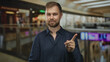 © Krakenimages.com - Man points finger to camera in shopping mall atrium wearing navy shirt and beard, indoor shopping center setting; confidence instruction guidance.