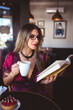 © Cavan Images - Woman drinking coffee and reading a book.