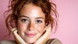 © Freshpixel - A cheerful young woman with beautiful freckles is smiling, posing with her hands on her cheeks against a soft pink background, emphasizing joy and positivity in youthful beauty.