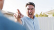 © Bonsales - Angry middle aged man shouting and pointing finger during an argument, expressing frustration and conflict outdoors