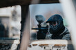 © qunica.com - A masked paintball player aims a marker through a dusty vehicle window, ready for action. The scene shows a tactical, sport-focused moment framed by the car’s frame.