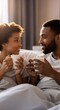 ©  Tsvyk L. - Young happy african american couple drinking morning coffee in bed while cheerfully talking and enjoying a cozy morning together at home.