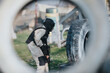© qunica.com - Paintball player in camouflage and mask crouches behind a large tire on an outdoor field. A dynamic scene of a paintball game with gear and barriers in view.
