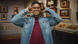 © Krakenimages.com - Hispanic man adjusts glasses and smiles while touching ears amid framed paintings in an art gallery building; joy wonder.