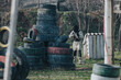 © qunica.com - A masked paintball player in beige protective suit holds a marker near a tire obstacle. The outdoor scene shows a rugged field with stacked tires and a shooter ready for action.