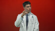 © Krakenimages.com - Man doctor wearing white coat and tie with closed eyes pointing finger with stethoscope in red studio; confidence.