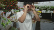 © Krakenimages.com - Man holds hands to eyes in binocular gesture at street flower shop with bouquet displayed on stall; curiosity.
