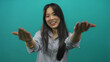 © Krakenimages.com - Young chinese woman pointing and gesturing 'come here' against an isolated green background wall, expressing a friendly and inviting demeanor in a casual setting.