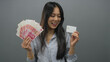 © Krakenimages.com - Woman holding chinese yuan banknotes and a credit card against an isolated grey background, showcasing financial prosperity and modern banking concepts.