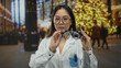 © Krakenimages.com - Woman doctor in white uniform adjusting eyeglasses in a vibrant street setting with holiday decorations, showcasing a blend of professionalism and festive atmosphere.