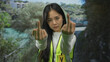 © Krakenimages.com - Woman wearing vest outdoors in park making gesture with middle fingers during daytime in vibrant green setting suggesting defiance or frustration captured in natural environment.