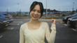 © Krakenimages.com - Young chinese woman smiling confidently in a parking area with cars outdoors under a cloudy sky, exuding a sense of joy and anticipation.