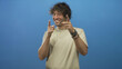 © Krakenimages.com - Young hispanic man points both index fingers and smiles, hands and wristwatch visible against blue backdrop in studio; playful.