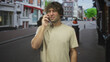 © Krakenimages.com - Man holds smartphone to ear with hand touching face on busy street lined with storefronts and trees; concern.
