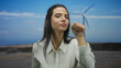 © Krakenimages.com - Hispanic woman in a white shirt simulating knocking and listening by a windmill in a vast outdoor field under a clear sky.