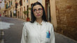 © Krakenimages.com - Woman scientist with glasses in uniform stands on a charming outdoor street, showcasing a thoughtful expression in a quaint urban setting.