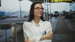 © Krakenimages.com - Young hispanic scientist woman in uniform stands outdoors at an airport looking concerned under a covered walkway holding her arms folded pens in pocket.