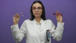 © Krakenimages.com - Hispanic woman optician in uniform with glasses against a purple wall demonstrates eyewear choices highlighting her professional setting.