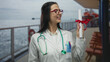 © Krakenimages.com - Hispanic woman doctor holding diploma on cruise ship deck with stethoscope, celebrating graduation outdoors during a voyage.
