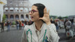 © Krakenimages.com - Hispanic woman doctor with stethoscope smiling and listening at the roman coliseum in an outdoor setting, blending professional attire with iconic historical architecture.