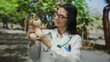 © Krakenimages.com - Young hispanic woman doctor in a park holding a stuffed toy with a stethoscope and wearing a uniform smiles outdoors in a green leafy setting.