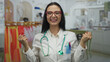 © Krakenimages.com - Young hispanic doctor woman with stethoscope smiling confidently inside clothing store full of colorful outfits