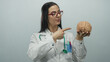 © Krakenimages.com - Hispanic female doctor with a stethoscope holds a brain model against a plain white wall background.