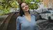 © Krakenimages.com - Woman smiling on a vibrant street in a blue blouse suggests happiness and freedom outdoors under green trees with bustling city life and traffic visible.