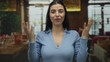 © Krakenimages.com - Young hispanic woman in blue expressing frustration indoors at a cozy restaurant setting with blurred background of dining area and décor.