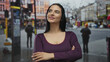 © Krakenimages.com - Young hispanic woman with crossed arms stands confidently on a bustling street with a red bus in the background, showcasing urban life and outdoor vitality.
