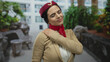 © Krakenimages.com - Woman flight attendant outdoors holding shoulder in pain wearing uniform with red scarf outdoors urban setting background with plants shows discomfort professional work.