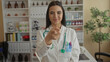 © Krakenimages.com - Young hispanic woman doctor smiling in clinic with stethoscope and white coat creating heart gesture, showing care and compassion in professional healthcare environment