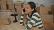 © Krakenimages.com - Young hispanic woman smiling while talking on phone surrounded by cardboard boxes and a drill inside her new home suggesting a recent relocation or renovation.