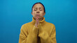 © Krakenimages.com - Woman praying with hopeful expression in yellow sweater against bright blue wall suggests anticipation and longing