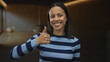 © Krakenimages.com - Woman smiling indoors showing thumbs up in a cozy room wearing striped sweater conveying positivity and confidence