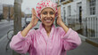 © Krakenimages.com - Young hispanic woman in a pink bathrobe and shower cap smiling outdoors on a city street showcasing cheerful morning freshness.