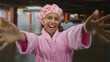 © Krakenimages.com - Woman in pink bathrobe with shower cap smiling in indoor parking lot near car, expressing joy, depicting a carefree lifestyle with a touch of humor and casual elegance.