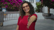 © Krakenimages.com - Woman wearing red shirt and glasses extends her hand for a handshake in a city street under bougainvillea blooms; warm connection.