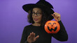 © Krakenimages.com - Woman holds a jack o lantern bucket by the handle and shows palm forward for a calm gesture in a purple studio; relaxation friendliness.