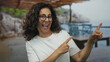 © Krakenimages.com - Middle-aged hispanic woman smiling and pointing at a beachside setting with rocky seaside views, conveying joy and relaxation outdoors.