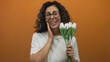 © Krakenimages.com - Middle-aged hispanic woman smiles holding white tulip bouquet against vibrant orange background.