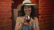 © Krakenimages.com - Woman in bikini and hat holding mug indoors at construction site, exuding happiness and relaxation in a unique setting with a red brick backdrop.