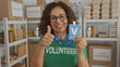 © Krakenimages.com - Woman in green volunteer shirt with badge in charity room giving thumbs up while smiling at camera indoors.
